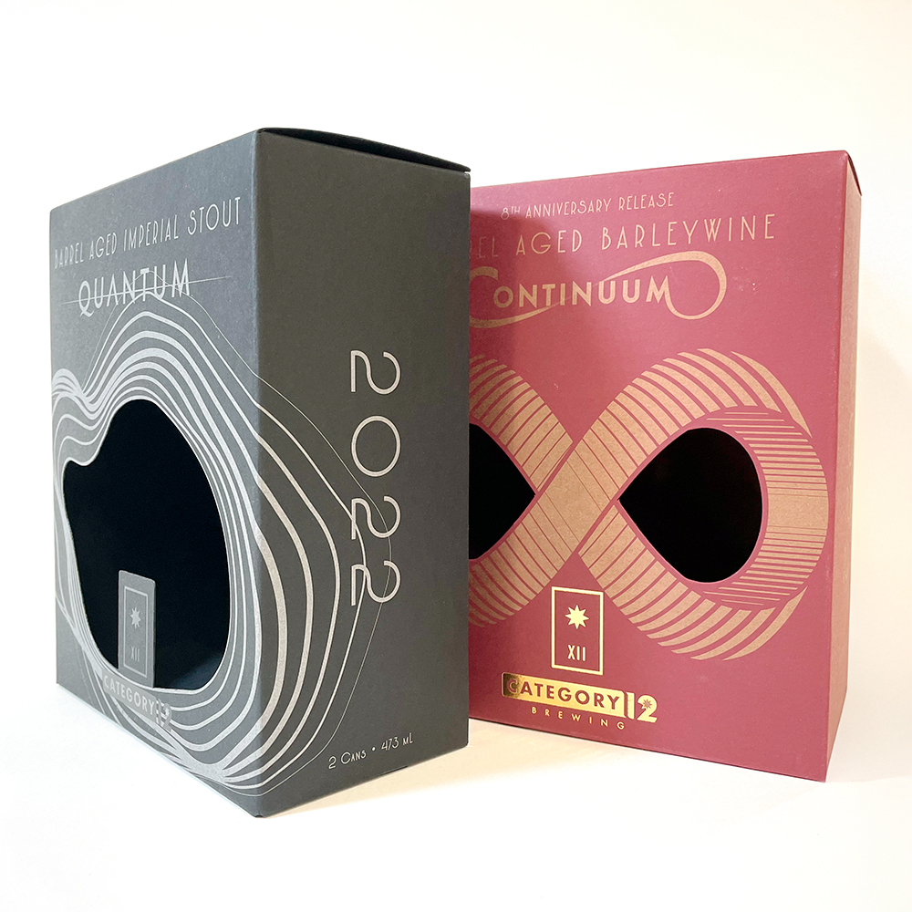 Two premium beer packaging boxes for Category 12 Brewing. The left box, labeled 'Quantum', is a dark matte finish with silver contour line artwork and a die-cut window. The right box, labeled 'Continuum', features a rich burgundy background with gold foil details and an infinity loop design around two oval windows. Both boxes highlight elegant typography and specialty print finishes