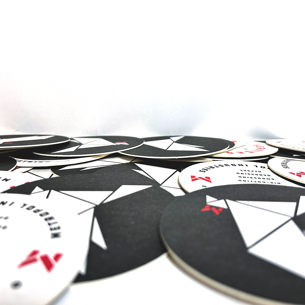 Stack of custom-printed round drink coasters featuring Metropol Industries’ geometric origami-style bird logo in black, white, and red. The design is clean and modern, printed on thick cardstock with a matte finish.